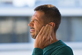 Otitis or tinnitus. Man touching his ear because of strong earache or ear pain.