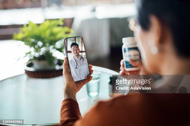 オンラインで医師と仮想予約を持つシニアアジアの女性, 自宅でスマートフォンで彼女の処方箋や薬の選択を相談.遠隔医療、高齢者、ヘルスケアの概念 - 健康診断 ストックフォトと画像