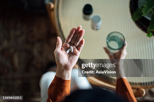 Vue aérienne d’une femme asiatique âgée se sentant malade, prenant des médicaments à la main avec un verre d’eau à la maison. Concept pour les personnes âgées et les soins de santé Vue aérienne d’une femme asiatique âgée se sentant malade, prenant des médicaments à la main avec un verre d’eau à la maison. Concept pour les personnes âgées et les soins de santé