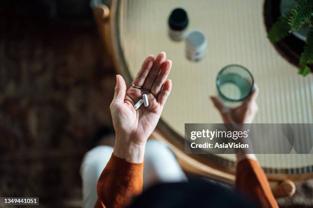 overhead view of senior asian woman feeling sick, taking medicines in hand with a glass of water at home. elderly and healthcare concept - slaappil stockfoto's en -beelden