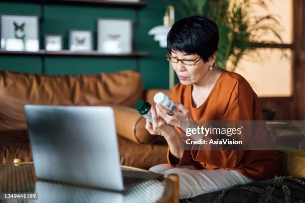 senior asian woman having a virtual appointment with doctor online, consulting her prescription and choice of medication on laptop at home. telemedicine, elderly and healthcare concept - pharmaceutical stockfoto's en -beelden