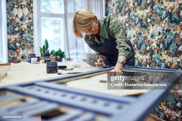 a woman paints a frame for a mirror in the workshop. - restoring art stock pictures, royalty-free photos & images