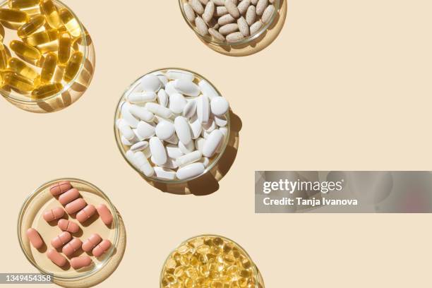 various pills and capsules, vitamins and dietary supplements in petri dishes on a beige background. flat lay, copy space - fish oil foto e immagini stock