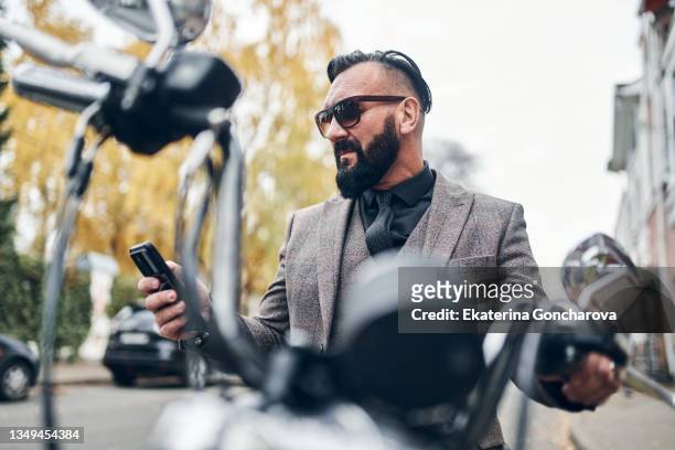 a man in a three-piece suit on a motorcycle with phone in the city. - adultes moto photos et images de collection
