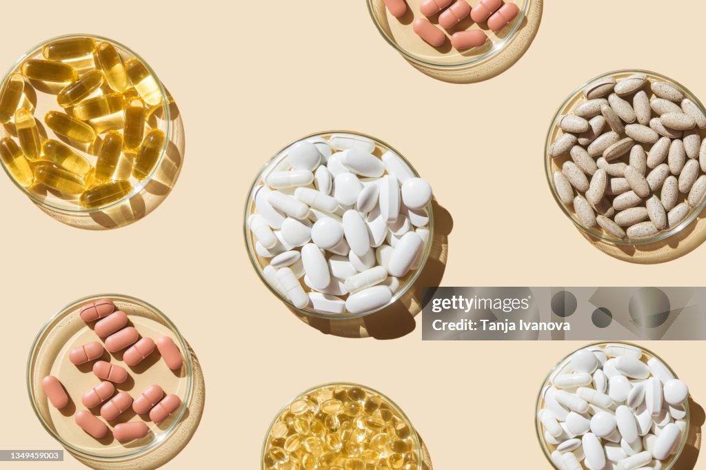 Various pills and capsules, vitamins and dietary supplements in petri dishes on a beige background.