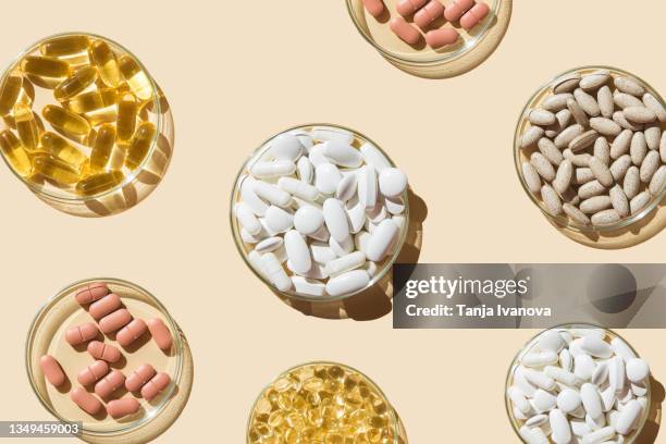 various pills and capsules, vitamins and dietary supplements in petri dishes on a beige background. - vitaminas fotografías e imágenes de stock