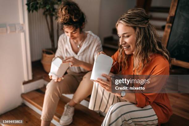 businesswomen eating food sitting on stairs during lunch break at office - chinese takeaway stock pictures, royalty-free photos & images