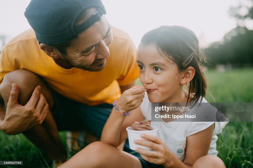 Cute young girl enjoying ice cream with her father in park