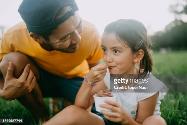 cute young girl enjoying ice cream with her father in park - gemengde afkomst stockfoto's en -beelden
