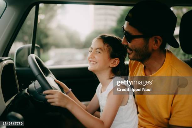 young girl pretending to drive car with her father at parking lot - véhicule terrestre photos et images de collection