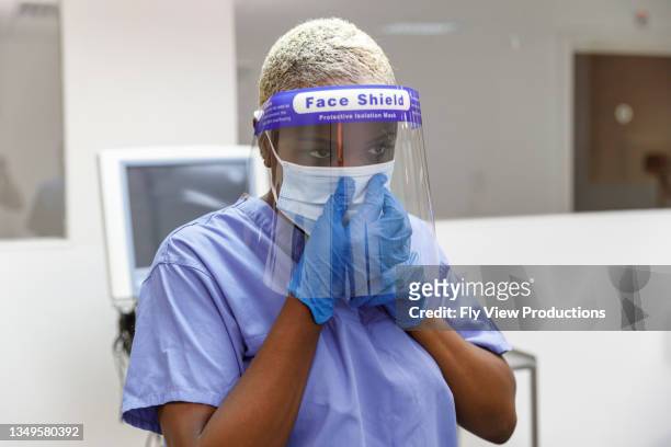 porträt einer schwarzen krankenschwester, die arbeitsschutzkleidung anstrickt - face shield stock-fotos und bilder