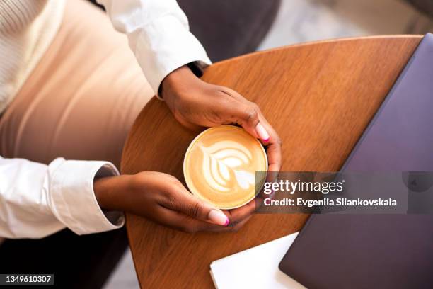 black businesswoman hands holding cup of hot coffee that standing on wooden table in cafe. - café au lait stock pictures, royalty-free photos & images