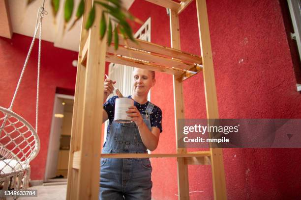happy woman painting wooden shelf on the balcony - painting house exterior stock pictures, royalty-free photos & images