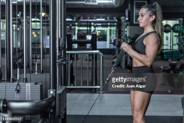 female athlete doing biceps cable curl exercise in the gym - bicep curl stockfoto's en -beelden