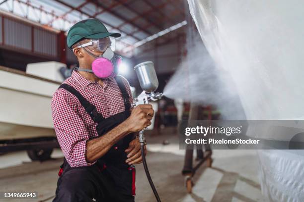 man using spray gun getting paint over boat body, maintenance of sailing yacht in workshop. - repairing boat stock pictures, royalty-free photos & images