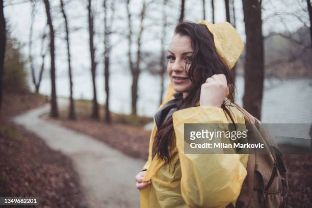 a happy young woman spends time in the woods on a rainy day enjoying nature, dressed in a yellow raincoat. - rain poncho stockfoto's en -beelden