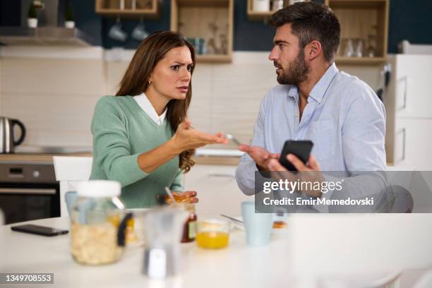 young woman looking irritated while her husband uses his phone during breakfast at home - cheating wives photos 個照片及圖片檔