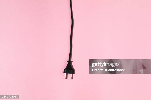black cable with male plug hanging on pink background. electric energy and renewable energy concept. - prise électrique photos et images de collection