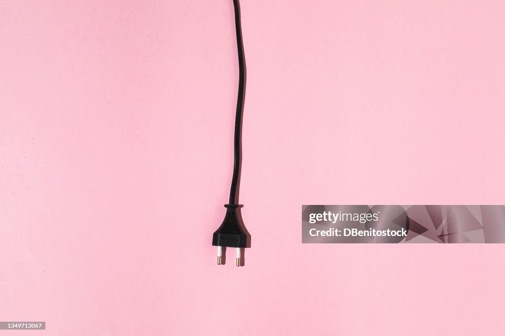 Black cable with male plug hanging on pink background. Electric energy and renewable energy concept.