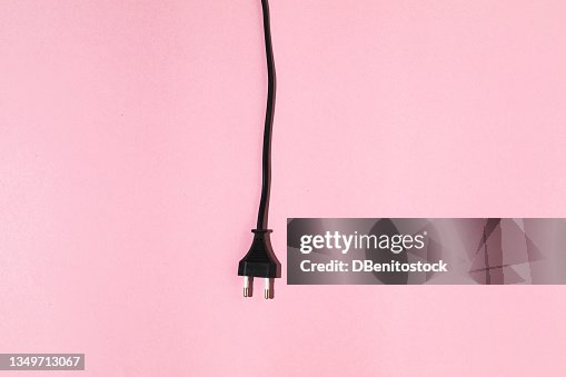 Black cable with male plug hanging on pink background. Electric energy and renewable energy concept. Black cable with male plug hanging on pink background. Electric energy and renewable energy concept.