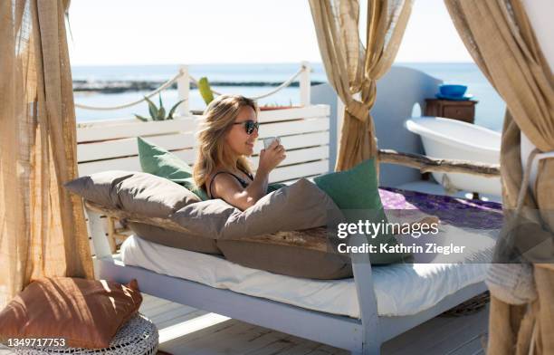 woman relaxing on daybed on a terrace with sea view, having coffee - sicily stock pictures, royalty-free photos & images