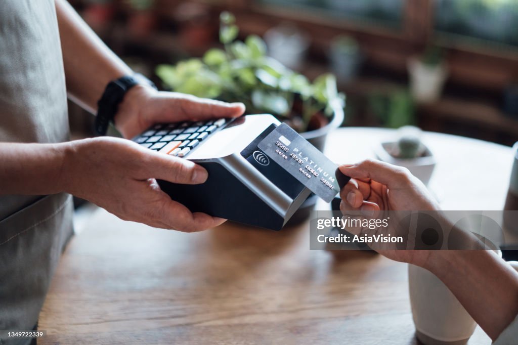 Nahaufnahme der Hand einer Frau, die in einem Café mit Kreditkarte rechnungsbezahlt und an einem Kartenautomaten scannt. Elektronische Zahlung. Banking und Technologie