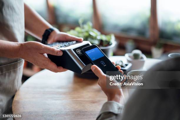 gros plan de la facture d’un homme payant à la main avec paiement sans contact par carte de crédit sur smartphone dans un café, numérisation sur une machine à cartes. paiement électronique. banque et technologie - asia stock photos et images de collection