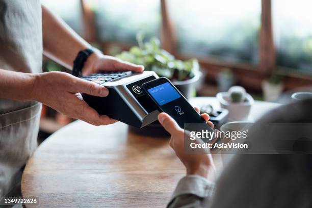 close up of a male's hand paying bill with credit card contactless payment on smartphone in a cafe, scanning on a card machine. electronic payment. banking and technology - paying stock pictures, royalty-free photos & images