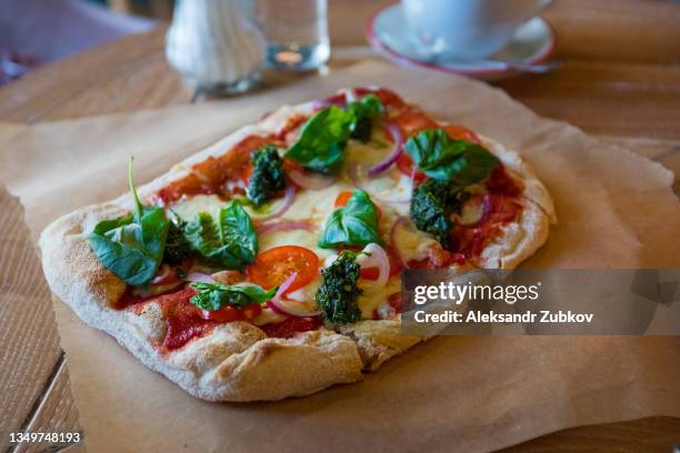 pizza margarita with cheese, ketchup or tomato paste, and basil leaves on a wooden stand or cutting board, on a table in a cafe or fast food restaurant. traditional italian cuisine in a pizzeria. vegetarian food. - tomato paste stock pictures, royalty-free photos & images