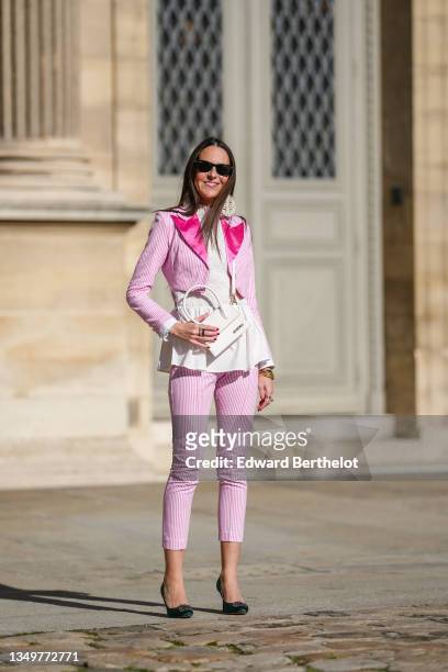 Alba Garavito Torre wears black sunglasses from Ray Ban, white cut-out pattern large pendant earrings, a white ruffled turtleneck shirt, a pink and...