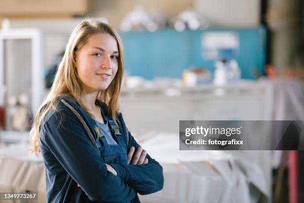 porträt einer lächelnden jungen auszubildenden in der metallindustrie, arme verschränkt - berufsausbildung stock-fotos und bilder