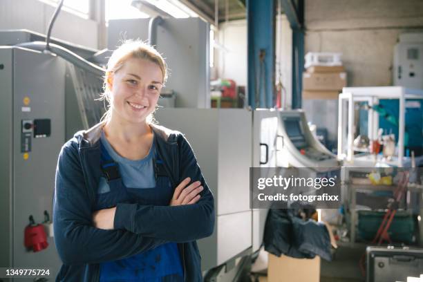 porträt einer lächelnden jungen auszubildenden in der metallindustrie, arme verschränkt - lehrling stock-fotos und bilder