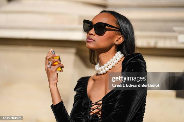 Emilie Joseph @in_fashionwetrust wears black sunglasses, diamond earrings, a white large pearls necklace, a black laces V-neck / shoulder-pad / long...