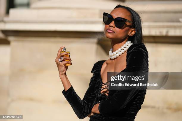 Emilie Joseph @in_fashionwetrust wears black sunglasses, diamond earrings, a white large pearls necklace, a black laces V-neck / shoulder-pad / long...
