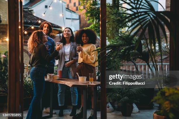 eine gruppe von freunden feiert eine aperitif-party auf einer großen terrasse bei sonnenuntergang - aperitif stock-fotos und bilder