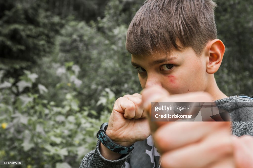 Boy fighter with a bruise on his face threatens with a fist