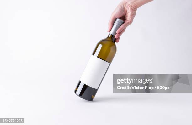 cropped hand of man holding bottle against white background - wijnfles stockfoto's en -beelden