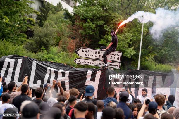 Protester waves a flare from a road sign during a march protesting the shooting of Nahel by a police officer in the Nanterre suburb of Paris, France,...