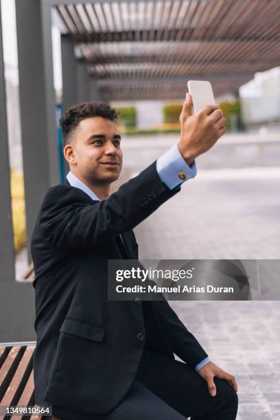 portrait of an enterprising young man in a mestizo suit sitting down and taking a selfie with his cell phone. - mensaje de móvil fotografías e imágenes de stock