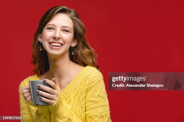 beautiful woman in studio is holding and drinking beverage from mug. concept with people on red background, person wear yellow jumper and smiling. girl with coffee or tea in the cup - adult woman cup tea stock pictures, royalty-free photos & images