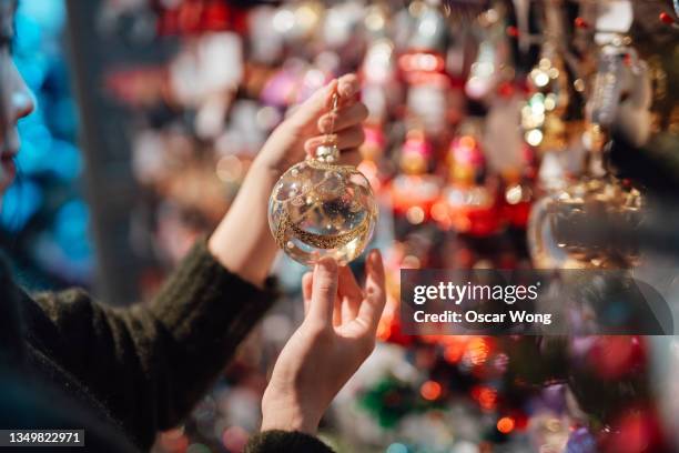 close-up of beautiful young asian woman choosing christmas ornaments at christmas market - hanging christmas lights stock pictures, royalty-free photos & images