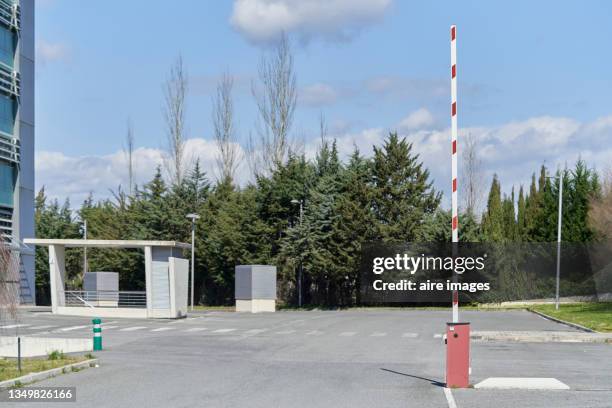 view of the exit of an asphalt parking with a barrier gate and some trees at background. a barrier gate has its arm in up position in a parking. - barricade stock pictures, royalty-free photos & images