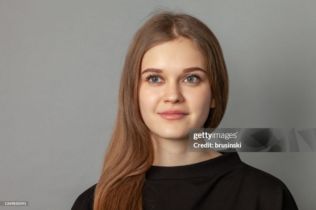 Close up studio portrait of attractive 19 year old woman with brown hair on gray background