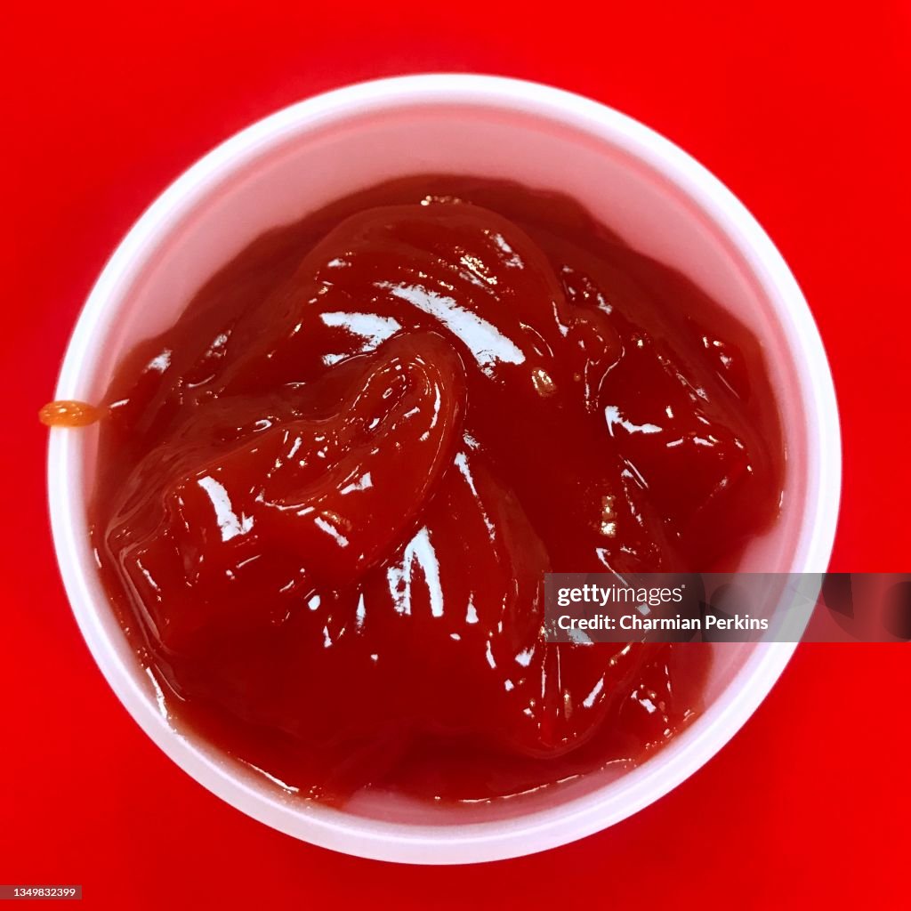 Close up of bright red tomato ketchup in pot, organic tomato sauce against red background, glossy shiny ketchup