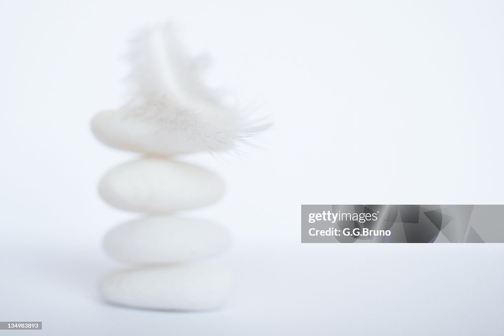 White feather laid on stack of white pebbles