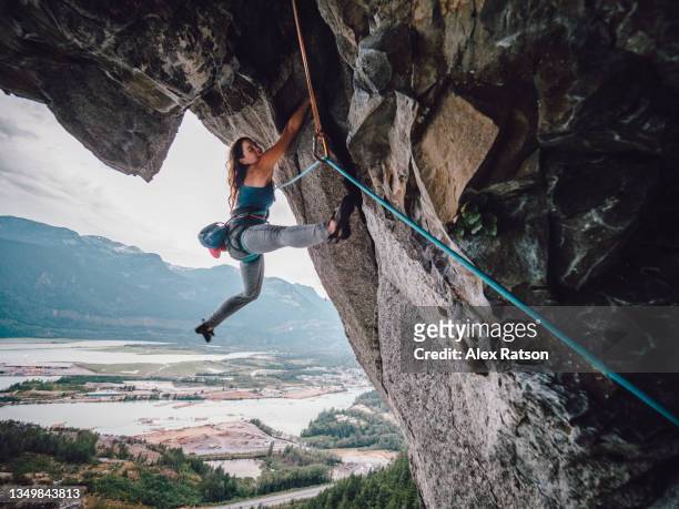 a female rock climber dances her way up a dramatic 500 meter tall rock face - overhangende rots stockfoto's en -beelden