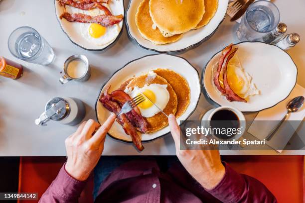 man eating pancakes with bacon and eggs in a traditional american diner, personal perspective overhead view - diner foto e immagini stock