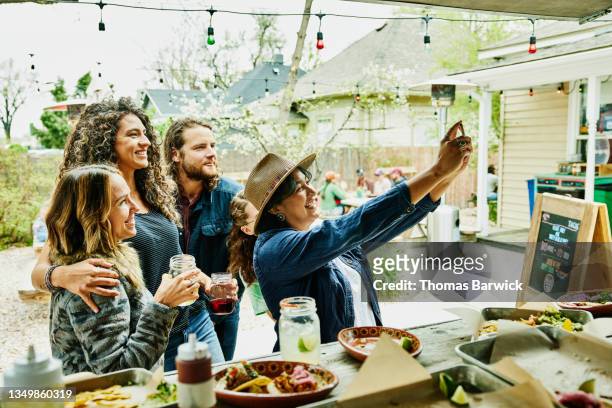 medium wide shot of friends taking selfie while dining together at food truck - millennials stock pictures, royalty-free photos & images