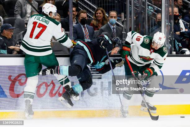 Brandon Tanev of the Seattle Kraken is upended by Marcus Foligno as Victor Rask of the Minnesota Wild takes the puck during the third period on...