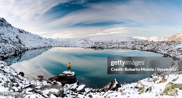 man standing on snowy mountain ridge by a frozen lake - pictured rocks in winter stock pictures, royalty-free photos & images